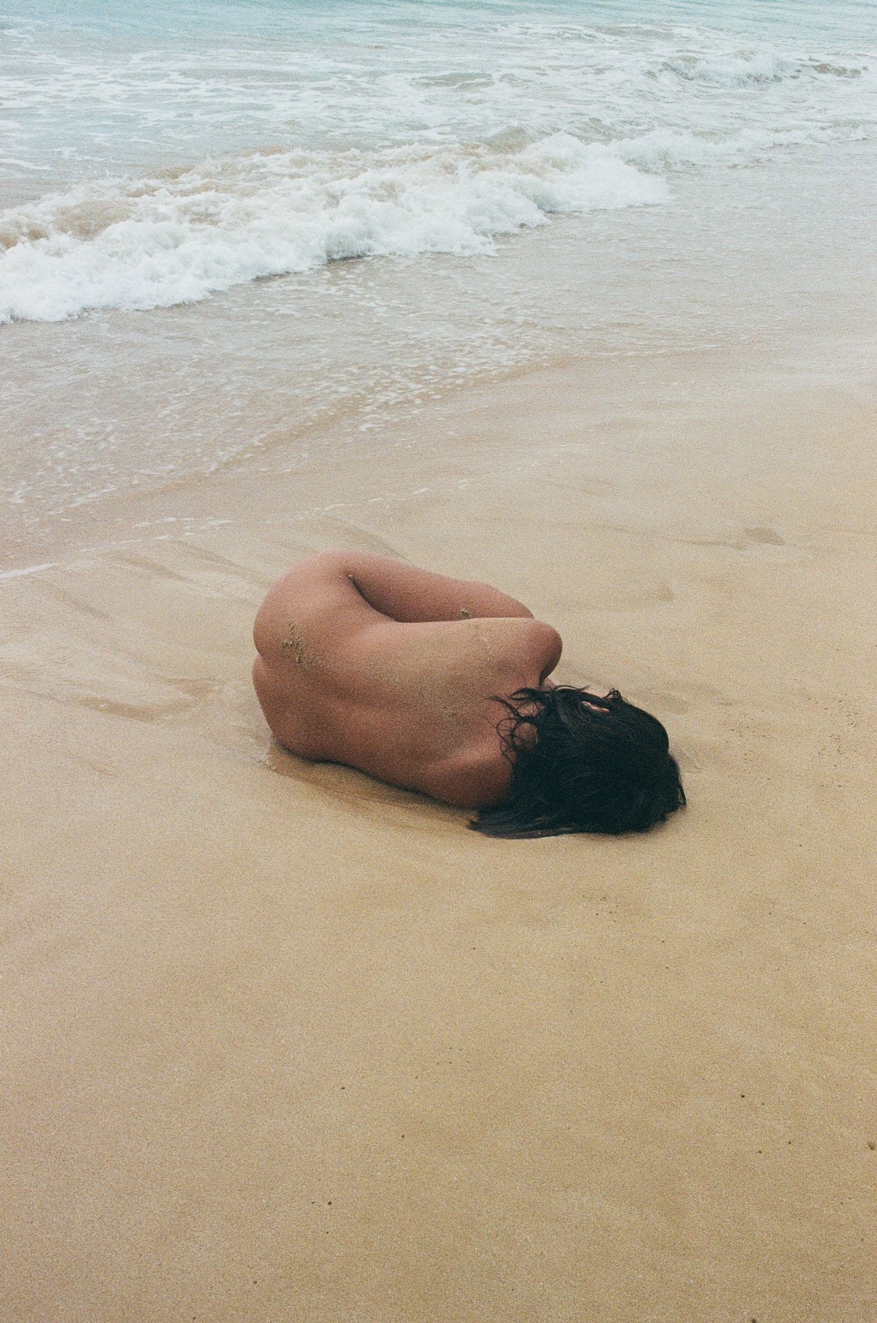 Figure curled on the shoreline